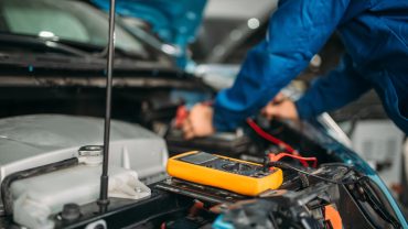 Car electrician with multimeter checks the battery level. Auto-service, vehicle wiring diagnostic