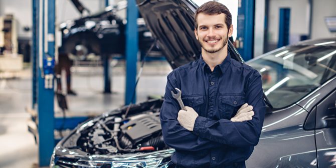 Auto car repair service center. Happy mechanic standing by the car